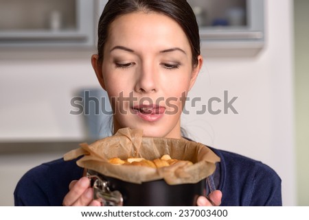 Happy young female cook holding a freshly baked apple cake or tart which she has just removed from the oven in a baking tin as she prepares dessert for dinner