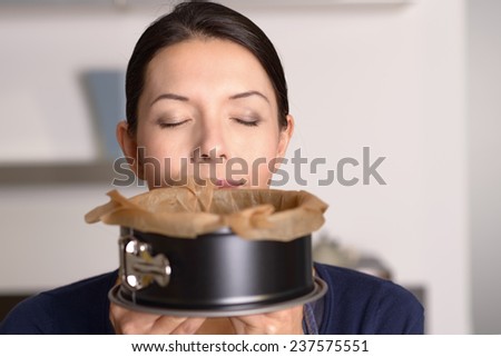 Attractive woman enjoying aroma of a freshly baked cake in a baking tin which she has just removed from the oven, concealing her lower face with closed eyes above
