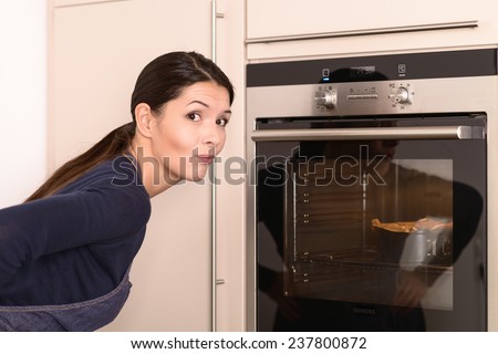 Pretty Young Woman Wearing Apron Waiting the Baked cake Near The Oven While looking at the Camera.