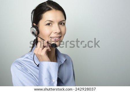 Attractive female call center operator, client services assistant or telemarketer wearing a headset looking at the camera with a charming friendly smile, on grey with copy space