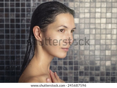 Attractive woman washing her hair in the shower rinsing it off under the spray of water looking away in a relaxed manner in a hair care, beauty and hygiene concept