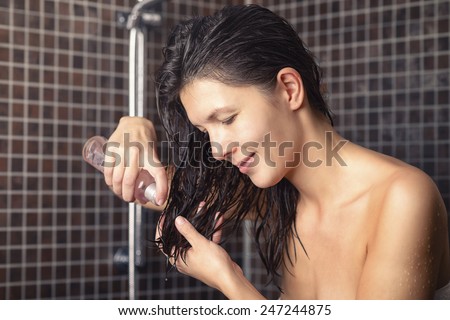 Young woman about to apply hair oil to her newly washed hair standing in the bathroom in a towel dispensing into her hand from the bottle