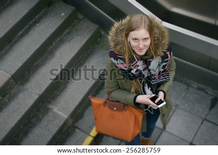 Aerial Shot of a Stylish Young Woman in Winter Fashion with Mobile Phone and Leather Bag, Pause for a Moment at the Stairs While Looking at the Camera.
