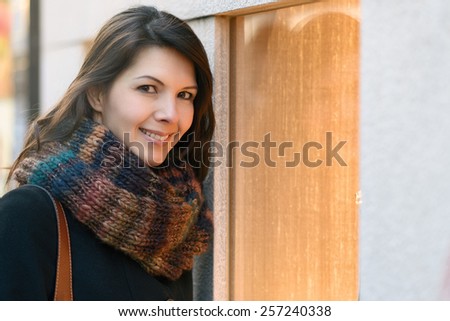Brunette attractive woman shopping in winter, in front of a store window, smiling at the camera