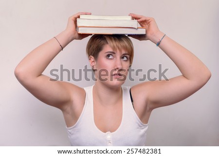 Close up Serious Young Woman with Short Blond Hair, Wearing Casual Sleeveless White Shirt, Balancing Books on her Head on a White Background.