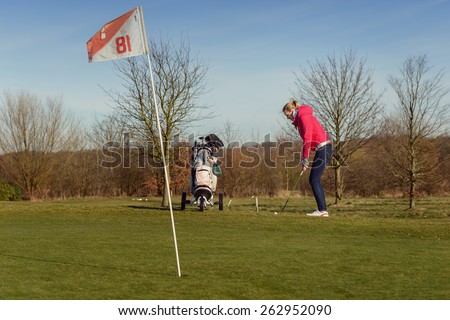 Young Female Golfer in a Golf Sports Training, Wearing Jacket and Jeans, chipping Golf Ball on Cup with Flag