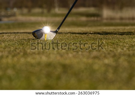 Conceptual image of a golfer teeing-off on the fairway with a low angle view of the ball on a tee and head of the driver on green grass with copy space
