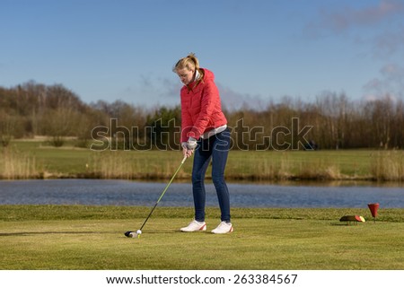Woman teeing of on a golf course standing in the tee box in front of a water hazard with a driver in her hands ready to make a distance stroke