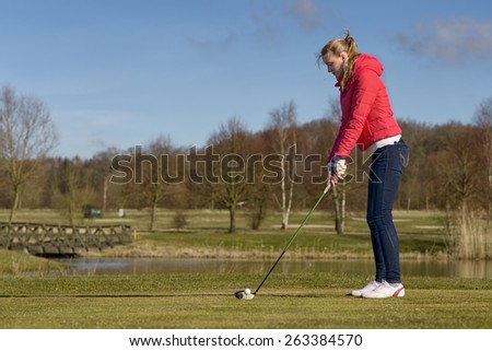 Woman teeing of on a golf course standing in the tee box in front of a water hazard with a driver in her hands ready to make a distance stroke