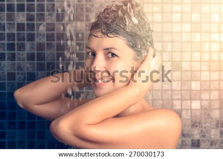 Woman shampooing her long brown hair under a shower working up a lather under the spray of water, view in profile