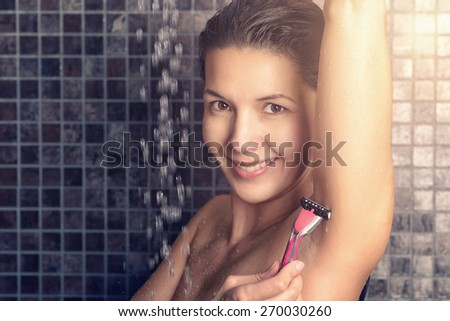 Smiling woman shaving her armpits in the shower with a pink disposable razor in a cleanliness and personal hygiene concept