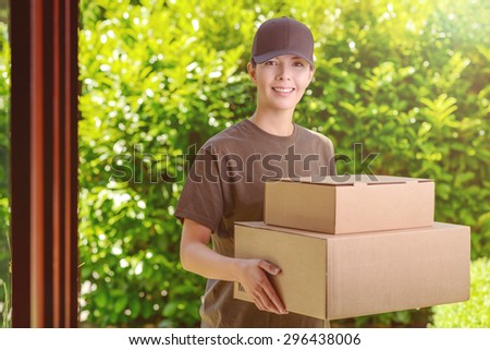 Attractive delivery woman or courier with two cardboard boxes in her arms standing waiting to make the delivery at a private house