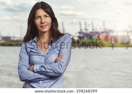 Half Body Shot of a Confident Pretty Young Woman Smiling at the Camera with Arms Crossing In Front her Body Against Hazy River Background.