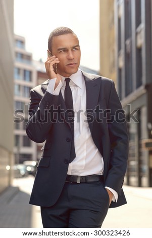 Three Quarter Shot of a Gorgeous Young Businessman Talking to Someone on his Mobile Phone While Walking In the Street and Looking Into the Distance.