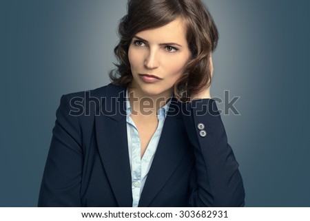 Attractive pensive woman sitting with her chin resting on her hand staring into space with a serious expression, over grey