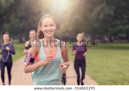 Half Body Shot of an Athletic Pretty Young Woman Smiling at the Camera While Jogging at the Park with Other Girls, with copy space on the right