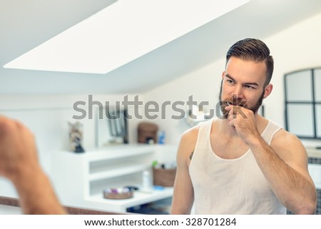 Attractive young bearded man brushing his teeth in the bathroom watching himself in the mirror in a dental hygiene concept