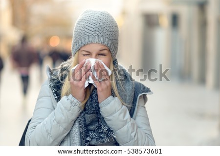 Woman with a seasonal winter cold blowing her nose on a handkerchief or tissue as she walks down an urban street in a health and medical concept