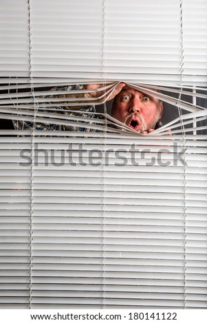 Agoraphobia. A man looking through a  window blind with facial expressions.