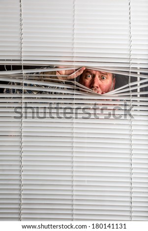 Agoraphobia. A man looking through window blinds with facial expressions.