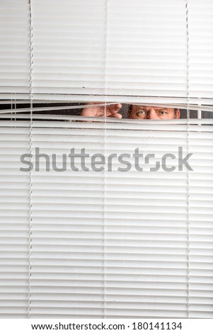 Agoraphobia. A man looking through rain spotted window blinds with facial expressions.