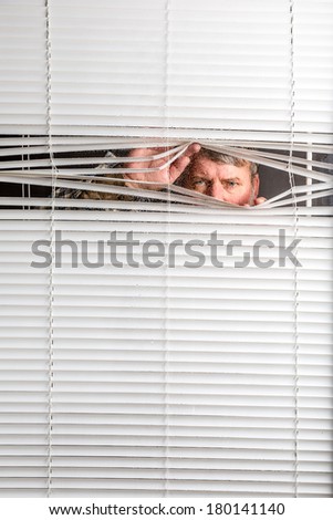 Agoraphobia. A man looking through  a rain spotted window blinds with facial expressions.