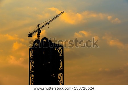 construction cane on top of cement industry building, silhouettes as  against a background of red sunset sky