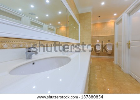wide angle shot of luxury empty restroom with granite washstands, mirror and urinal row