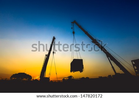 mobile crane lifting generator, silhouettes at sunset