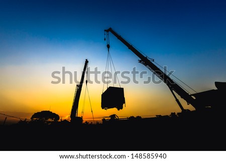 mobile crane lifting generator, silhouettes at sunset