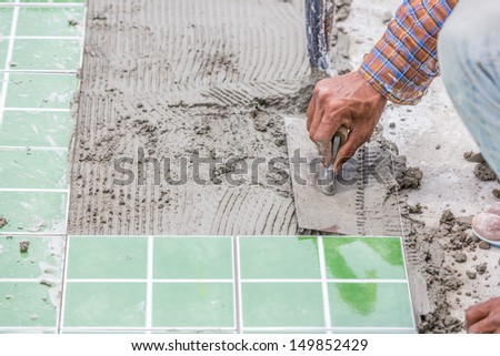 handyman spreading glue on the floor for laying green tiles on the floor