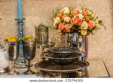 ariticial red and white roses arrangement in the vase the with tray cups , silver cups on the table