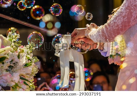 bride and groom cut the wedding cake with sword, with the background of bubbles.