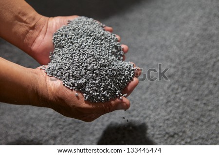Man\'s hands holding a pile of plastic pellets, gray colored