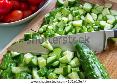 sliced cucumbers on the cutting board and knife, in the background the tomatoes in a bowl