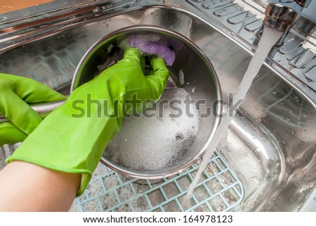 woman in green rubber gloves washing dishes in the sink under water