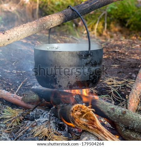 pot hanging over the fire in the forest in a hike, the water vapor from the boiler