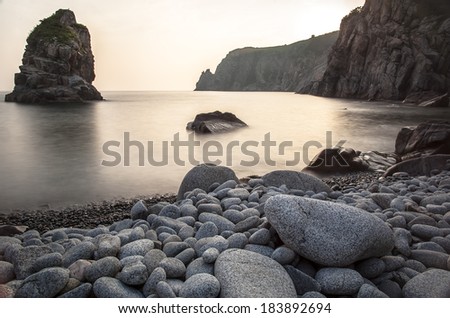 horizontal landscape the cliff coast with pebbles, large round stones and a huge rock at sunset