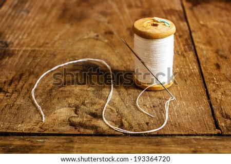 coil with white threads and a needle stuck standing on an old wooden table