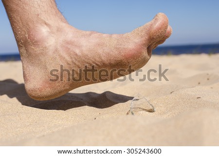Man goes on the beach and the risk of stepping on a splinter of broken bottle glass, which is lying on the sand littered in places with poor environmental conditions. Side view