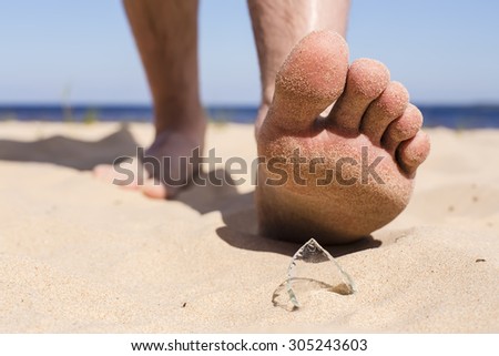 Man goes on the beach and the risk of stepping on a splinter of broken bottle glass, which is lying on the sand littered in places with poor environmental conditions