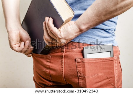 in the back pocket of jeans is an e-book, a man tries to shove in a second pocket thick old paper book