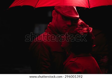 Couple standing in the rain under red umbrella