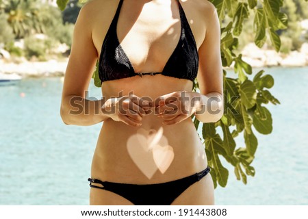 young female posing at beach with love heart shadows on her belly