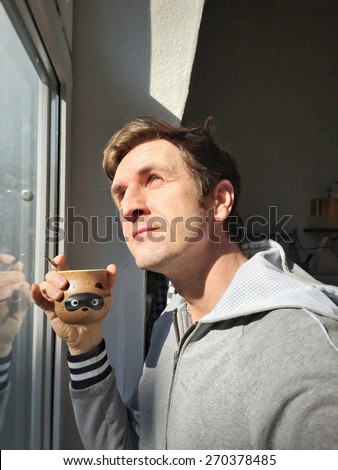 Young Caucasian man in casual drinking hot coffee next to window