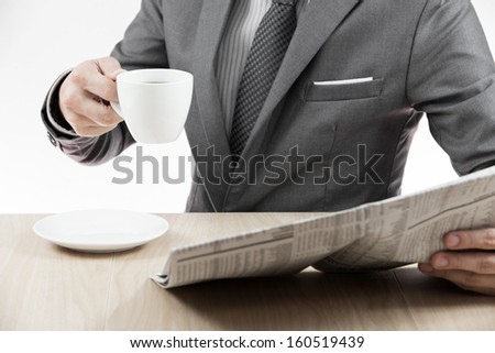 Businessman holding a cup of coffee and reading a newspaper on table