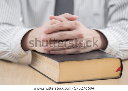 hands praying with bible on table