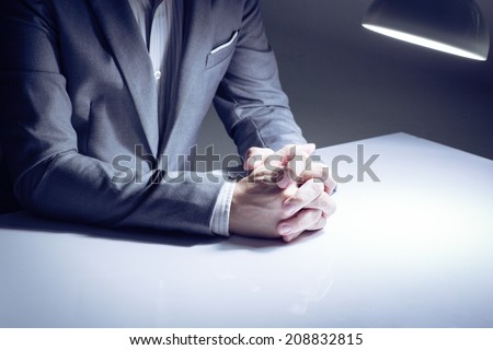 close up of a man in a suit with his hands clasped in front