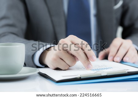 Businessman at the workplace drink coffee and looking some business papers with charts