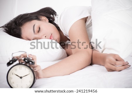 Woman in bed trying to wake up with alarm clock